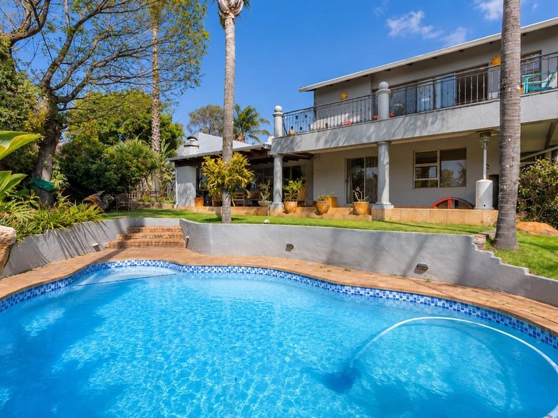 A well-maintained backyard featuring a swimming pool with tiled surround, a covered patio, and an upper-level balcony with wrought iron railings.