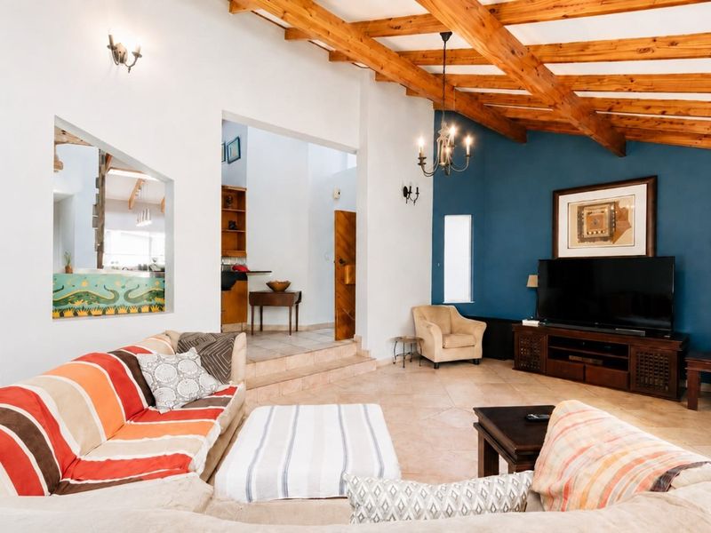Spacious living room featuring exposed timber ceiling beams, tiled flooring, and a raised transition area leading to an adjacent space.