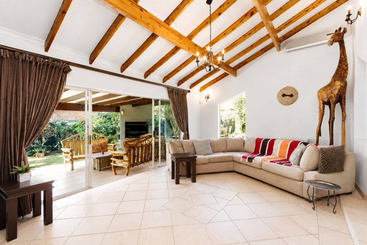 Spacious living room featuring exposed timber ceiling beams, tiled flooring, and large sliding glass doors that provide seamless access to the outdoor patio area.