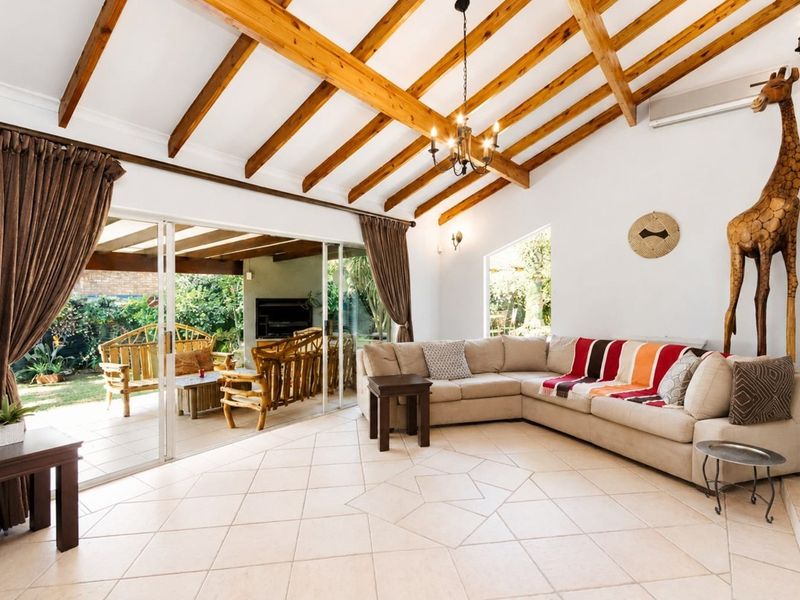 Spacious living room featuring exposed timber ceiling beams, tiled flooring, and large sliding glass doors that provide seamless access to the outdoor patio area.