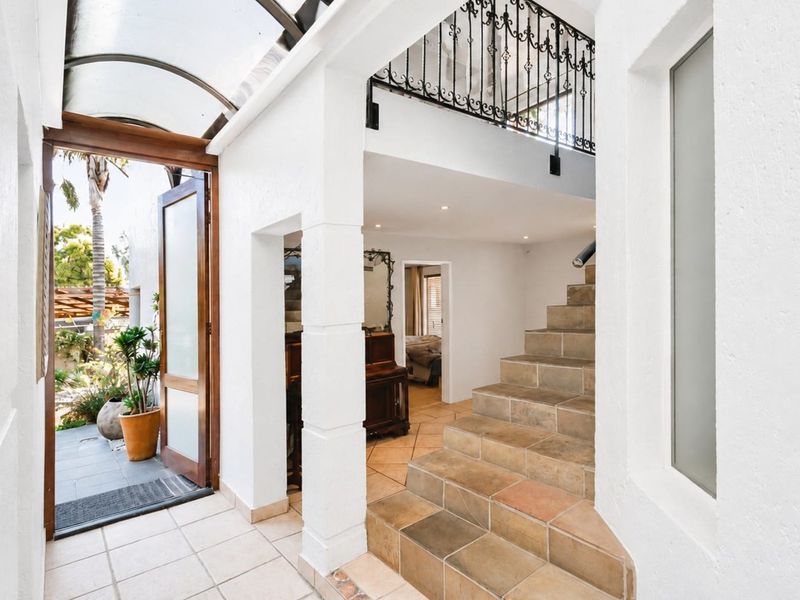 Bright entrance hall featuring a tiled staircase with wrought iron balustrade, recessed lighting, and an arched glass roof leading to the outdoor area.