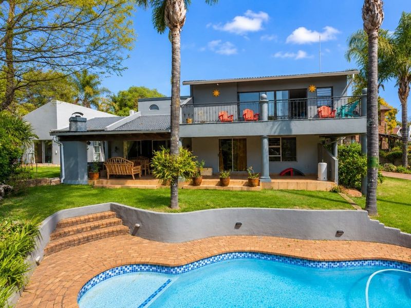 Rear view of the property featuring a swimming pool, brick paved surround, covered patio area, and an upper-level balcony with wrought iron railings.