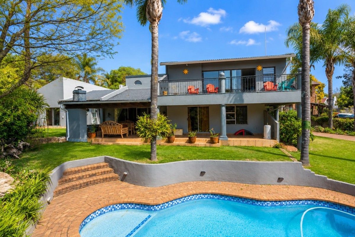 Rear view of the property featuring a swimming pool, brick paved surround, covered patio area, and an upper-level balcony with wrought iron railings.