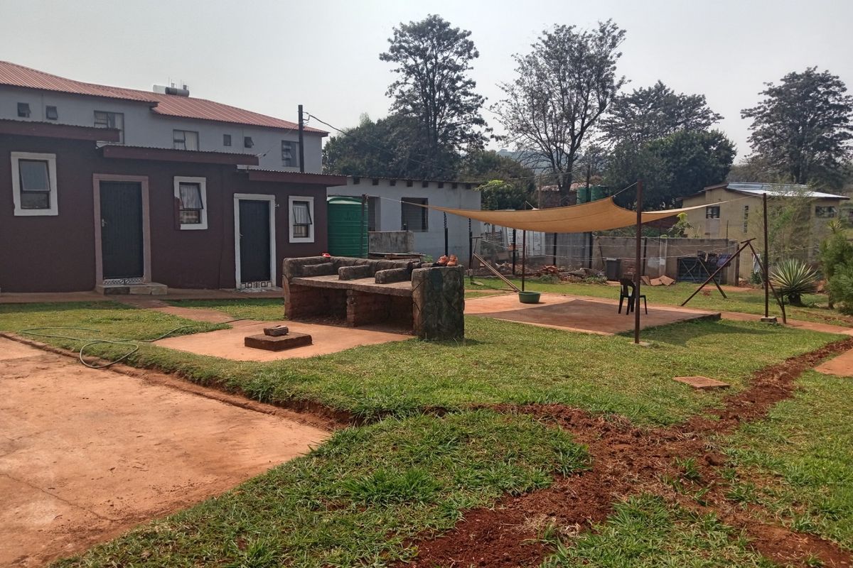 Rear exterior view featuring a built-in brick braai, a shade sail over a concrete patio area, and a water storage tank.