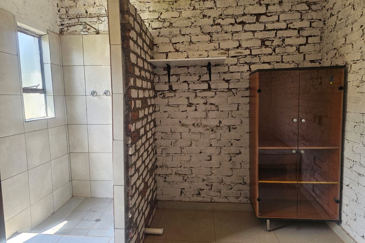 A bathroom featuring an exposed brick wall, a tiled shower enclosure, and tiled flooring, currently in need of finishing and cosmetic updates.