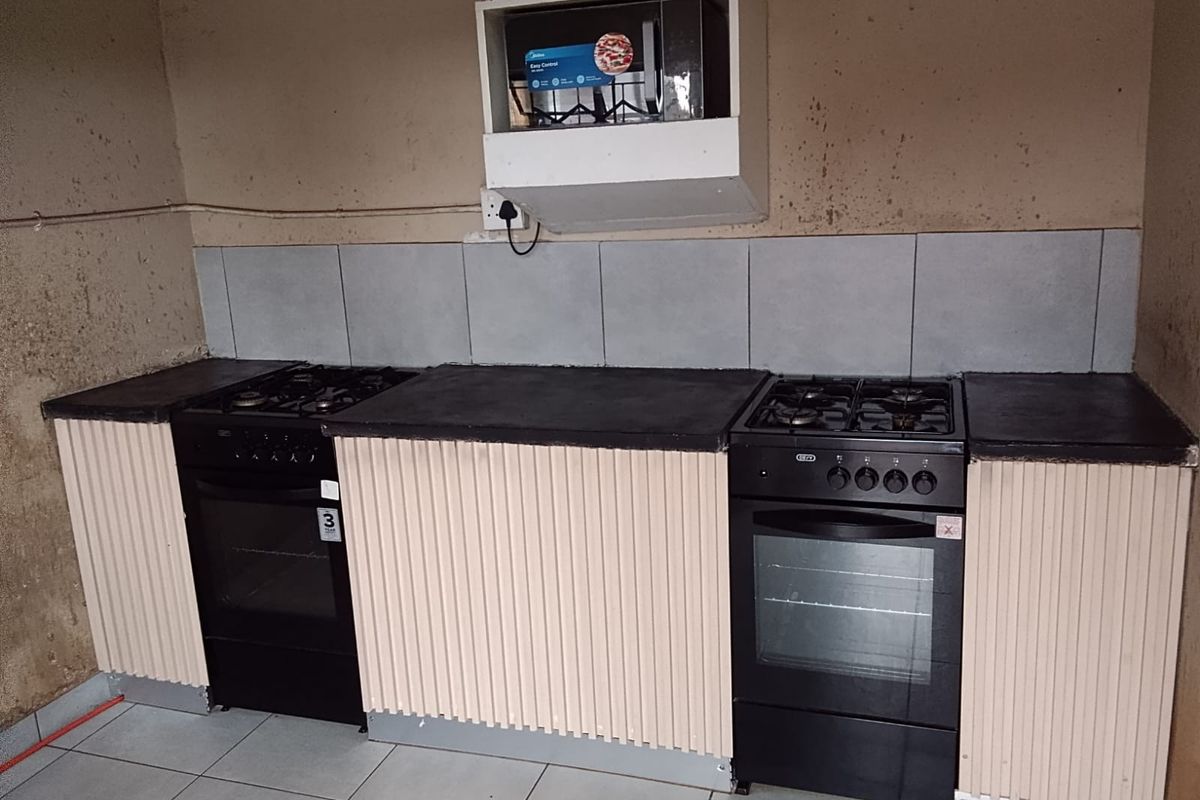A compact kitchen area featuring two freestanding ovens, tiled backsplash, and a built-in microwave, requiring wall repairs and cosmetic updates.