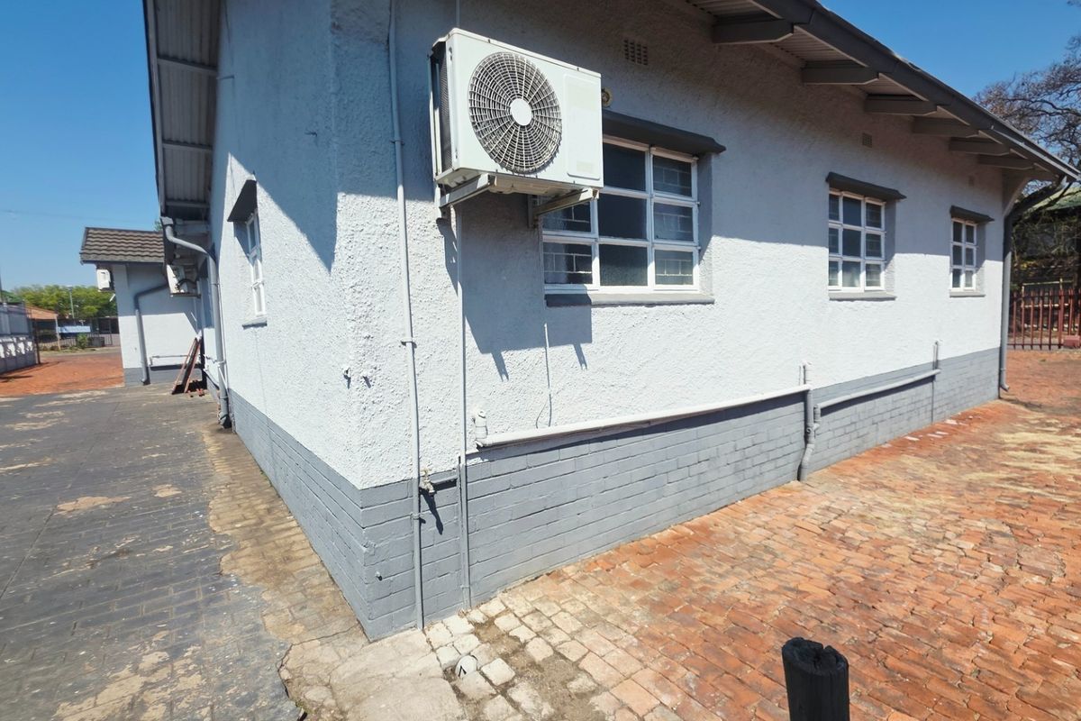 Rear exterior view of the property featuring painted brick walls, an installed air conditioning unit, and paved outdoor areas.