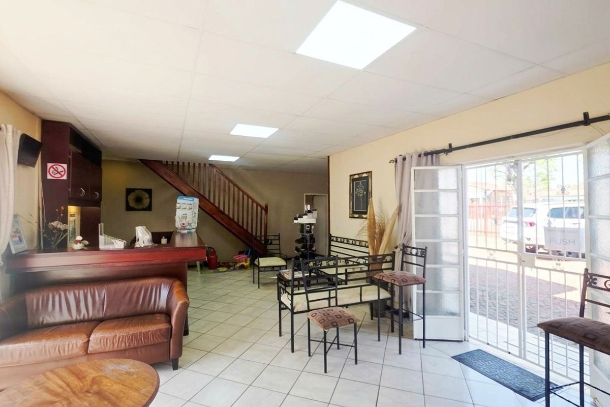 Open-plan living area featuring a built-in bar, wooden staircase, tiled flooring, and direct access to the exterior through a security gate.