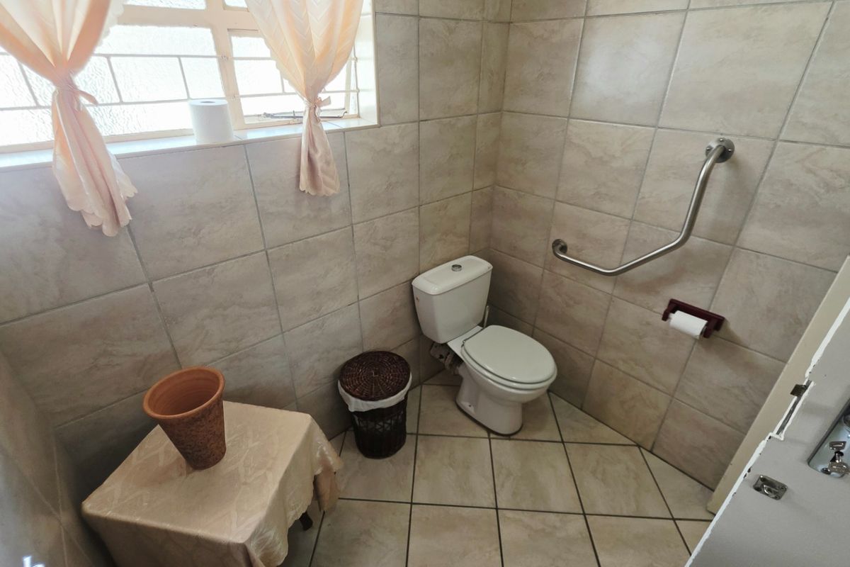 A functional bathroom featuring ceramic wall and floor tiles, a standard toilet, and a safety grab rail installed for accessibility.