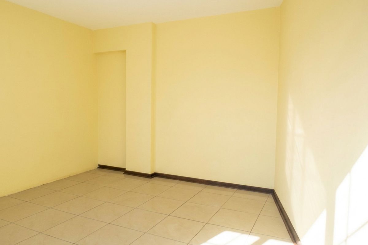 A vacant bedroom featuring neutral yellow walls and tiled flooring, offering a blank canvas for personalization.
