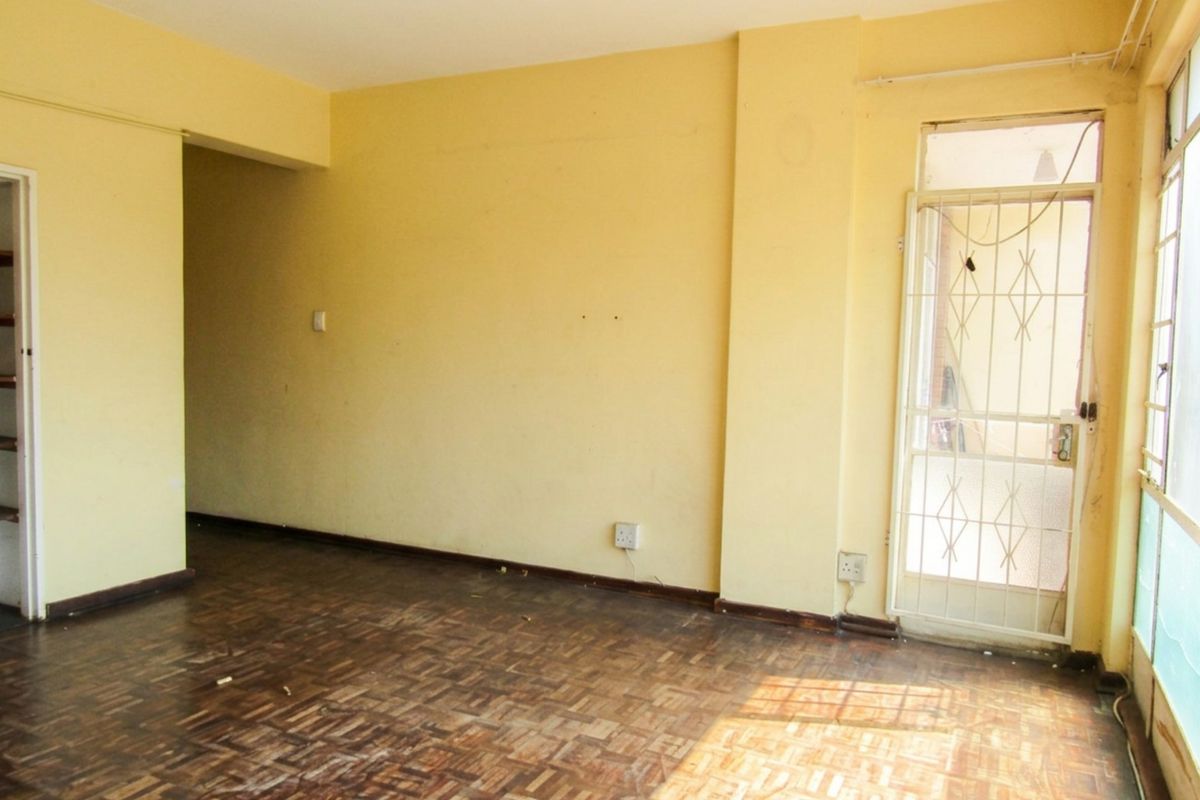 An empty living room featuring original parquet flooring, yellow painted walls, and a security gate leading to an outdoor area.