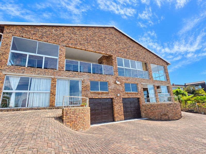 A multi-level face brick residence featuring a paved driveway, double garage, and upper-level balcony with glass balustrades.