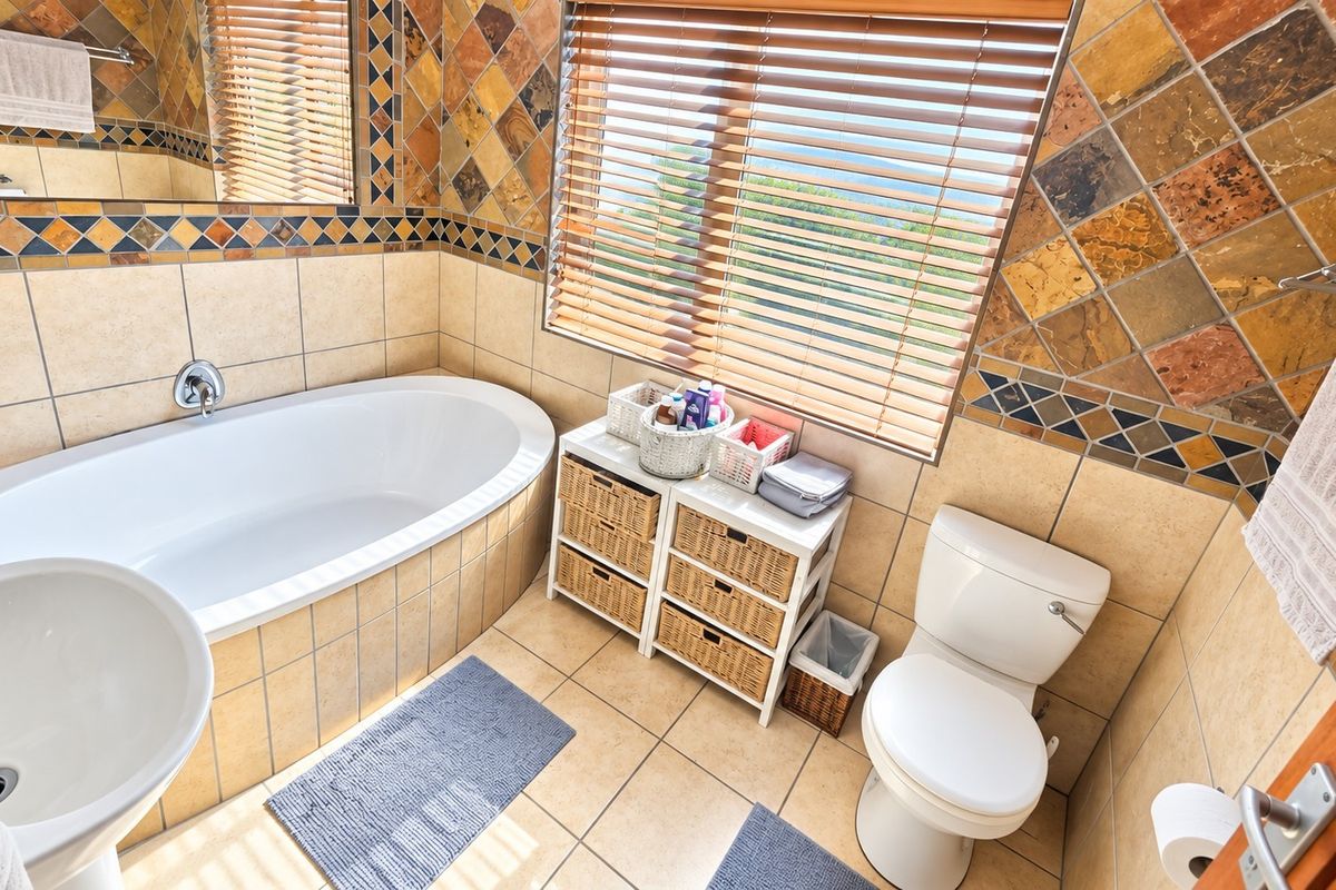 A functional bathroom featuring a built-in bathtub, pedestal sink, toilet, and decorative tiled wall accents with natural light from the window.