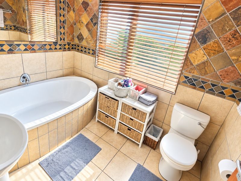 A functional bathroom featuring a built-in bathtub, pedestal sink, toilet, and decorative tiled wall accents with natural light from the window.