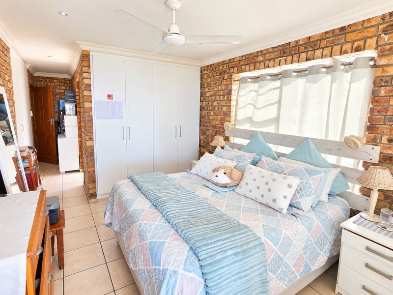 A well-lit bedroom featuring exposed brick walls, built-in cupboards, tiled flooring, and a ceiling fan.