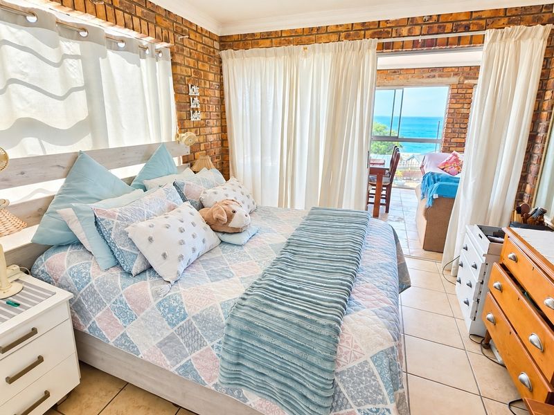 A bedroom featuring exposed brick walls and tiled flooring, with direct access to a balcony offering ocean views.