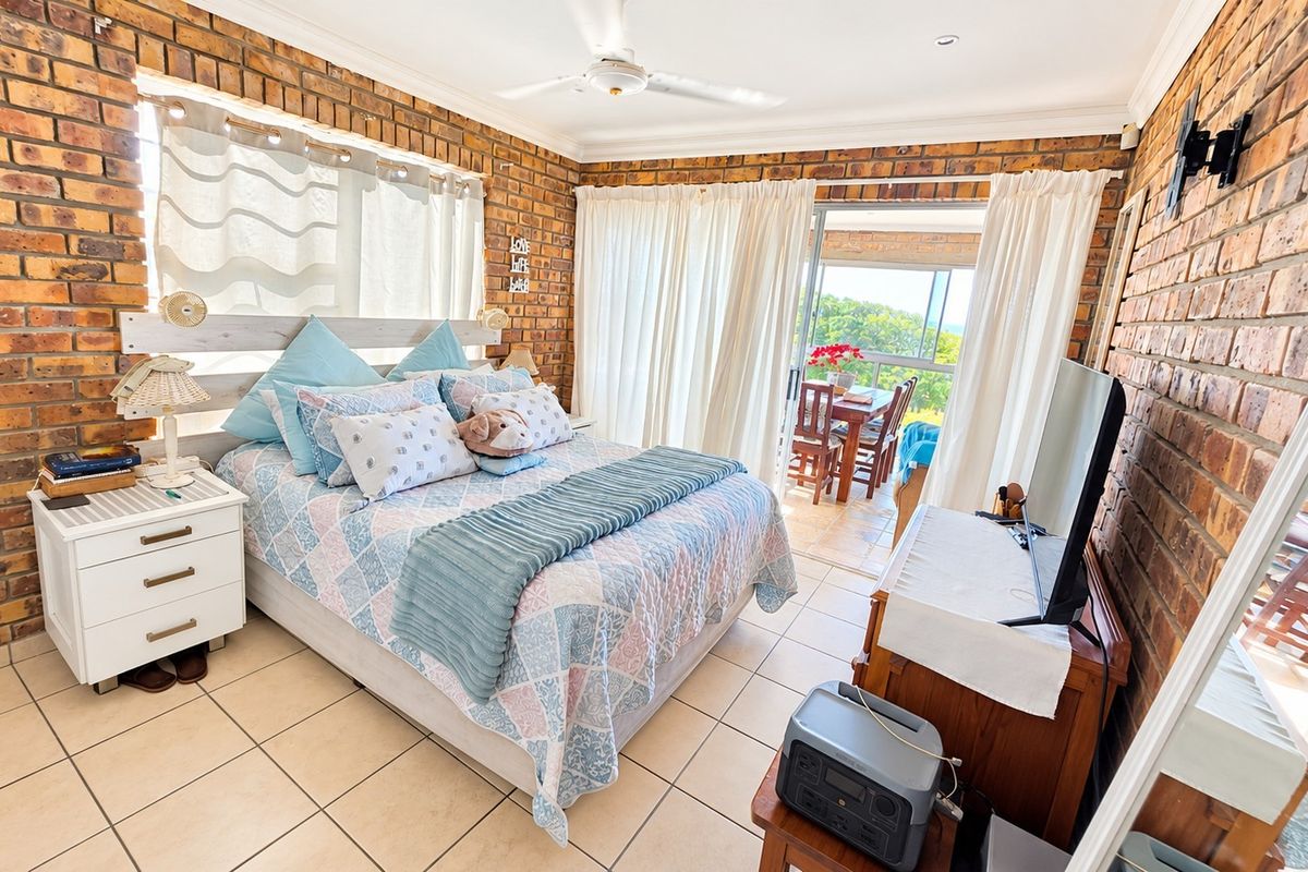 Spacious bedroom featuring exposed brick walls, tiled flooring, and sliding glass doors that open onto a private balcony with scenic views.