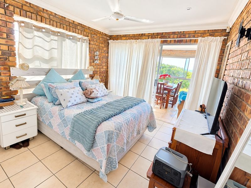Spacious bedroom featuring exposed brick walls, tiled flooring, and sliding glass doors that open onto a private balcony with scenic views.