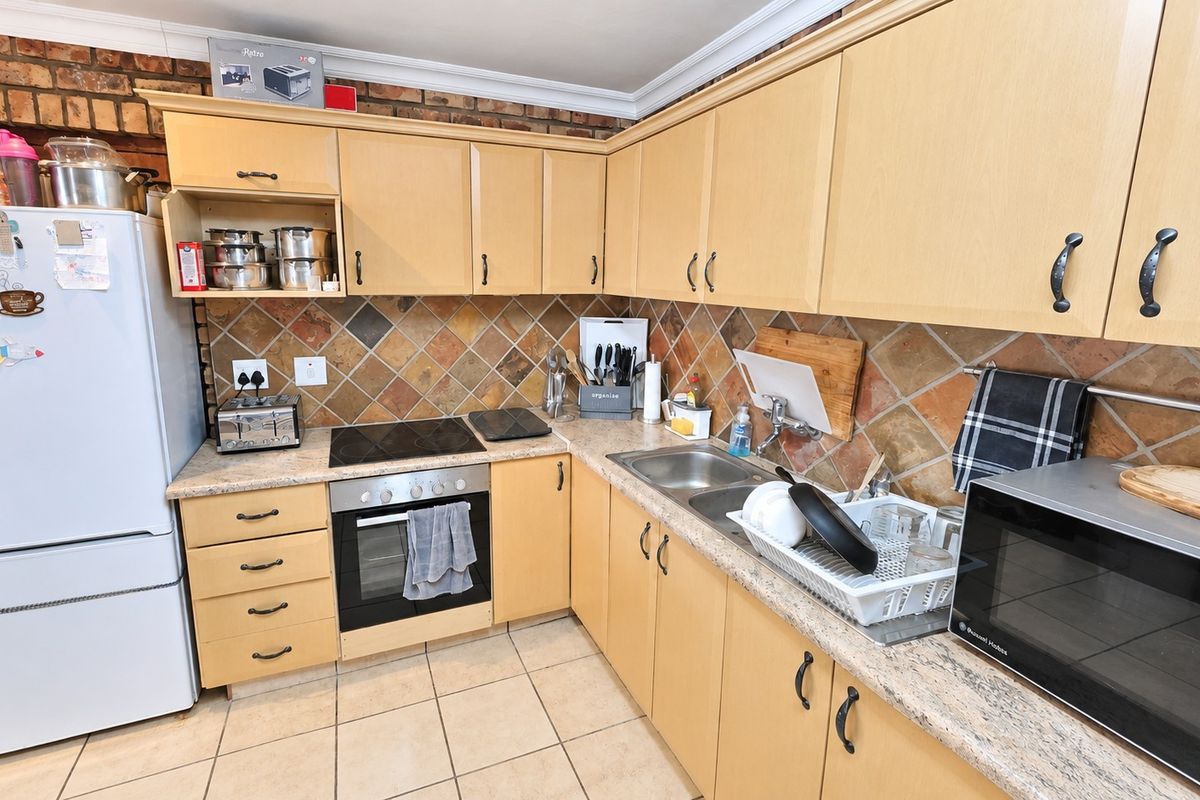 A functional kitchen featuring light wood cabinetry, a tiled backsplash, exposed brick accents, and integrated cooking appliances.