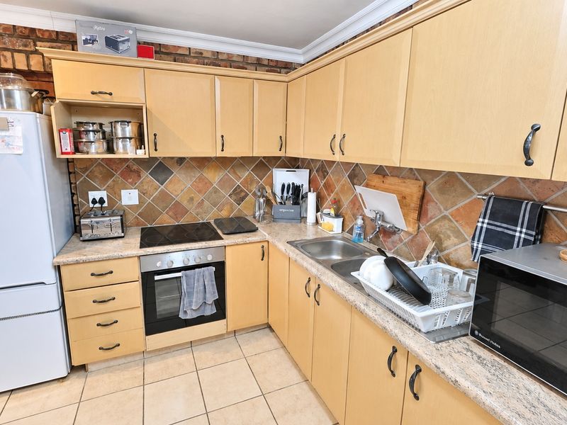 A functional kitchen featuring light wood cabinetry, a tiled backsplash, exposed brick accents, and integrated cooking appliances.