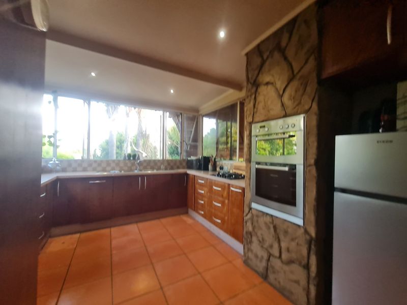 A functional kitchen featuring wooden cabinetry, a stone-clad oven housing, tiled flooring, and large windows providing ample natural light.