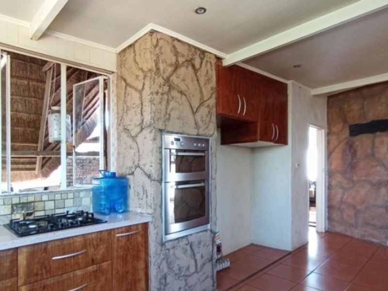 Kitchen featuring wooden cabinetry, built-in double oven, gas hob, and a distinctive stone-clad feature pillar, with tiled flooring throughout.