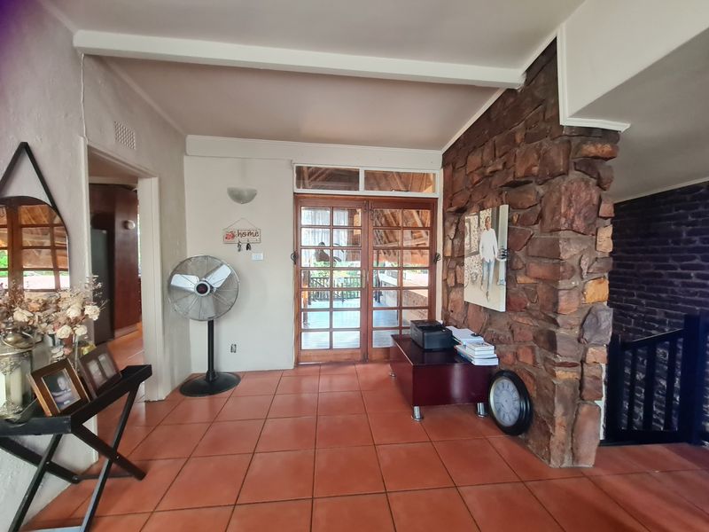 Entrance hall featuring terracotta floor tiles, a prominent stone feature wall, and timber-framed glass doors leading to an outdoor area.