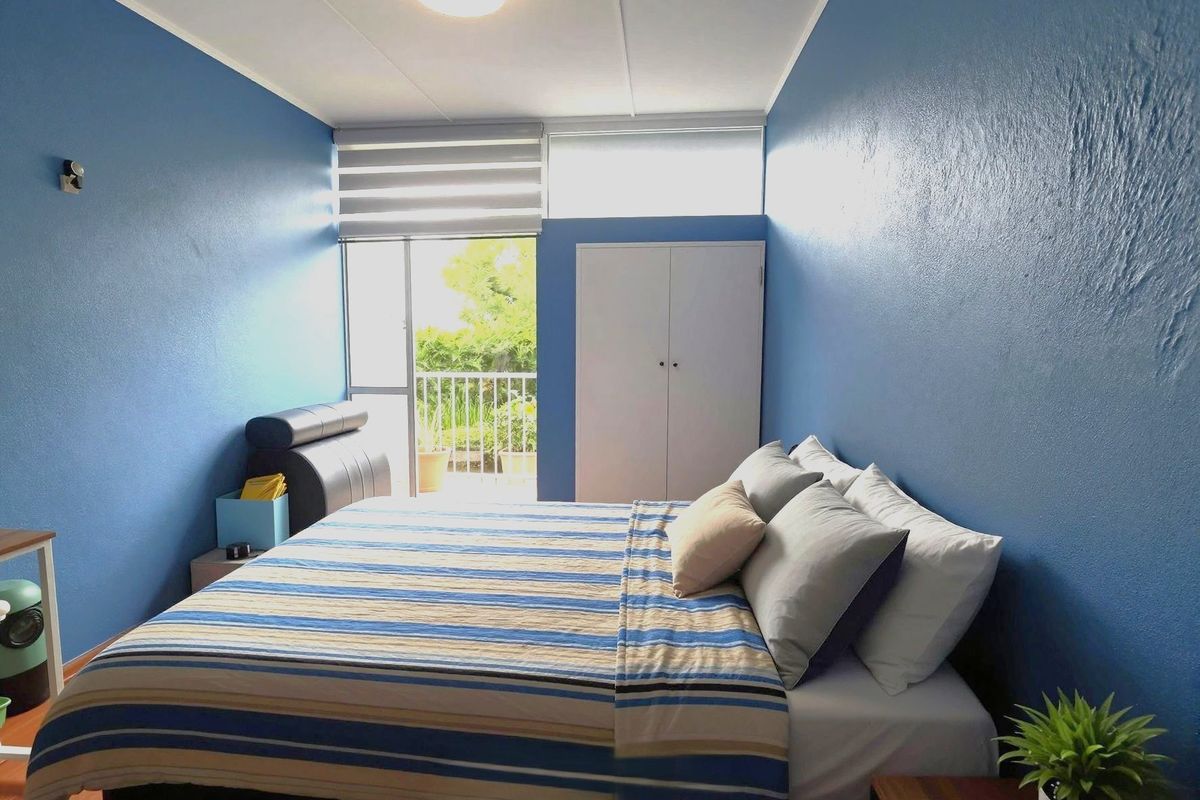 A bedroom featuring blue walls, a built-in wardrobe, and a sliding glass door providing access to a private balcony.