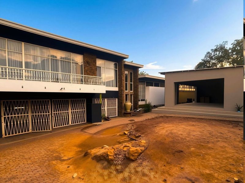 Rear view of the property featuring a multi-level structure with a balcony, security gates, and a covered patio area overlooking an unlandscaped garden.