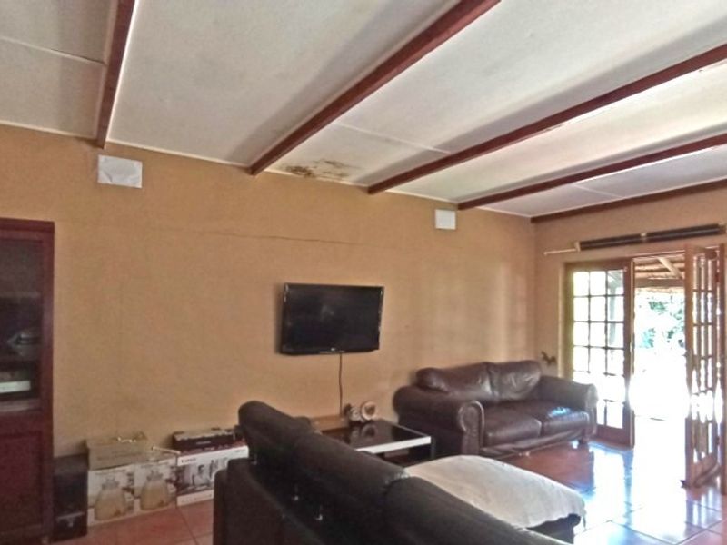 Living room featuring exposed timber ceiling beams, tiled flooring, and french doors leading to an outdoor area. Shows signs of ceiling water damage.