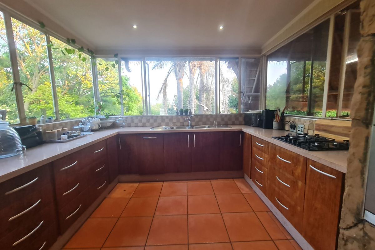 A U-shaped kitchen featuring wooden cabinetry, a gas hob, double sink, and large windows providing ample natural light and garden views.