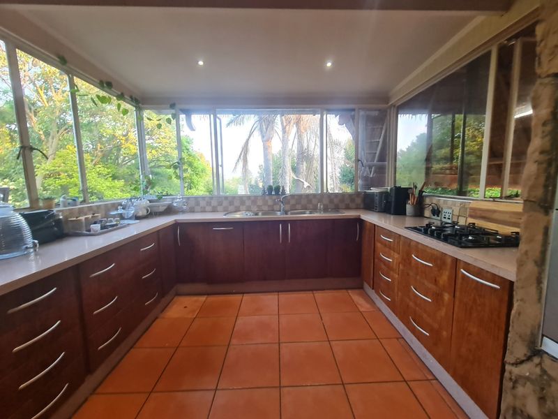 A U-shaped kitchen featuring wooden cabinetry, a gas hob, double sink, and large windows providing ample natural light and garden views.