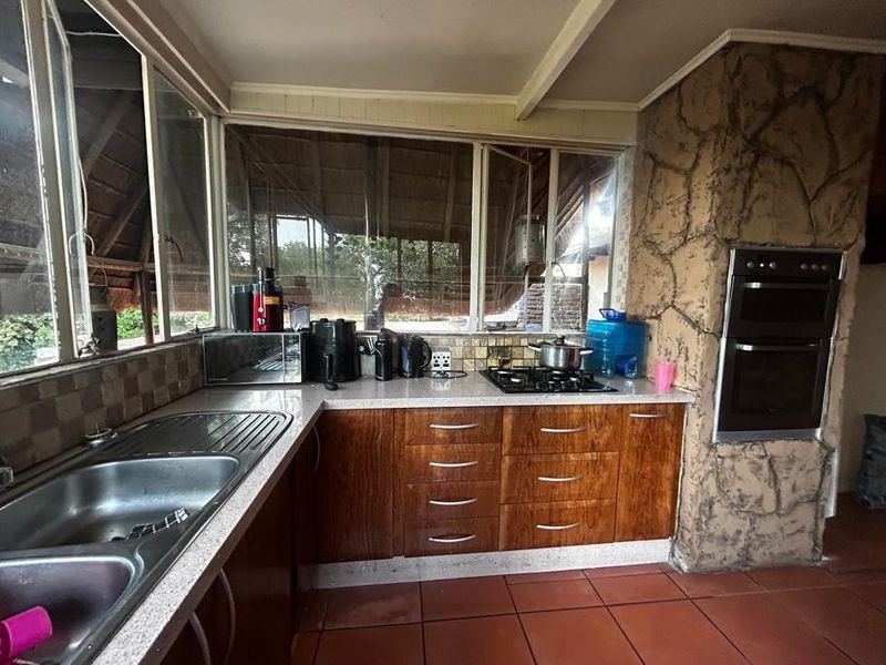 Kitchen featuring wooden cabinetry, a gas hob, built-in double oven, and a distinctive stone-clad feature wall with large windows overlooking the outdoor area.