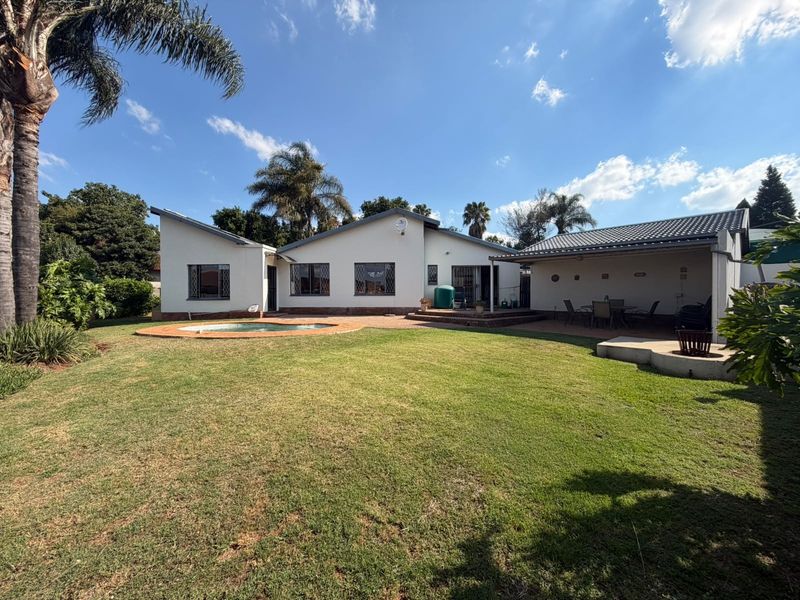 Rear view of the property featuring a swimming pool, a covered patio area, and a spacious garden with established trees.