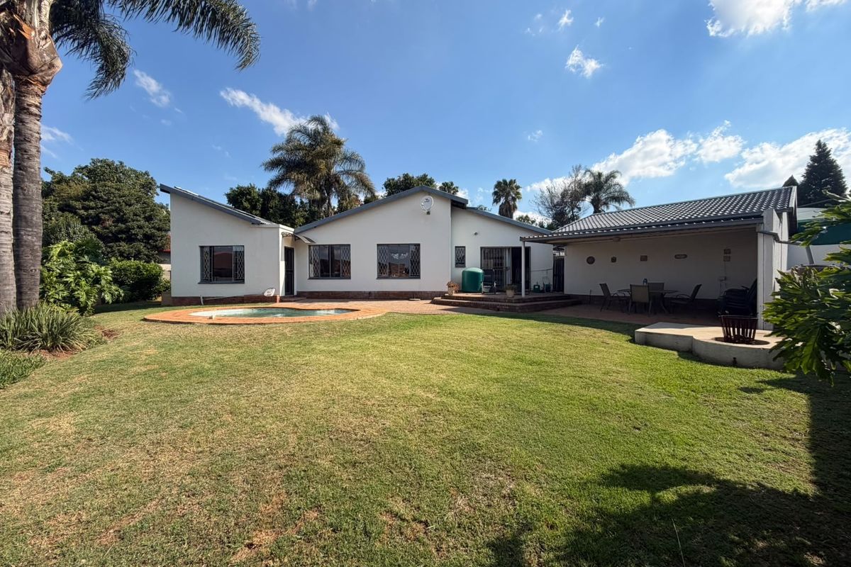 Rear view of the property featuring a swimming pool, a covered patio area, and a spacious garden with established trees.