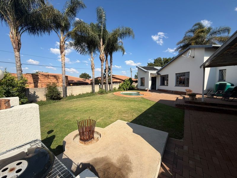 Spacious rear garden featuring a paved patio, a swimming pool, and a concrete fire pit area, perfect for outdoor entertaining.