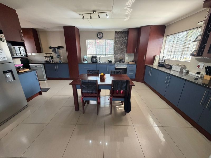Spacious kitchen featuring dark blue and wood-toned cabinetry, granite countertops, tiled flooring, and integrated appliances, offering a functional and well-lit cooking space.