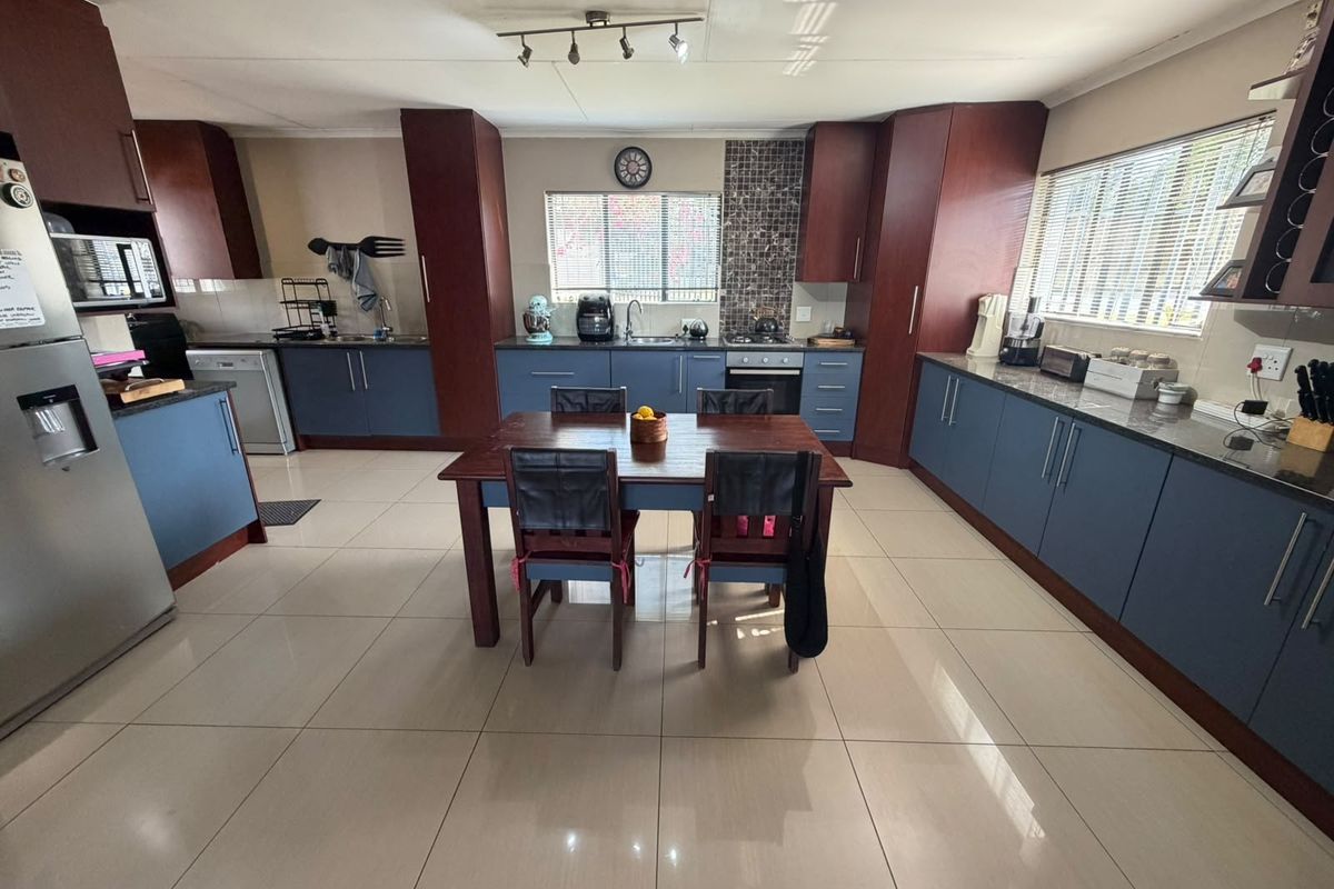 Spacious kitchen featuring dark blue and wood-toned cabinetry, granite countertops, tiled flooring, and integrated appliances, offering a functional and well-lit cooking space.
