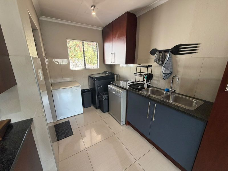 A functional laundry room featuring tiled flooring, granite countertops, a double stainless steel sink, and ample built-in cabinetry for storage.