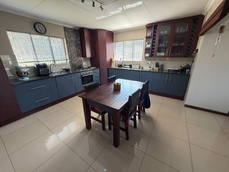 Spacious kitchen featuring dark blue and wood-toned cabinetry, mosaic tile backsplash, integrated oven, and tiled flooring with a central dining area.