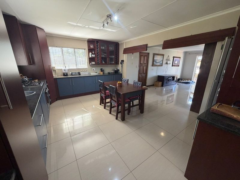 Spacious open-plan kitchen and dining area featuring dark wood cabinetry, granite countertops, gas hob, and polished tiled flooring throughout.
