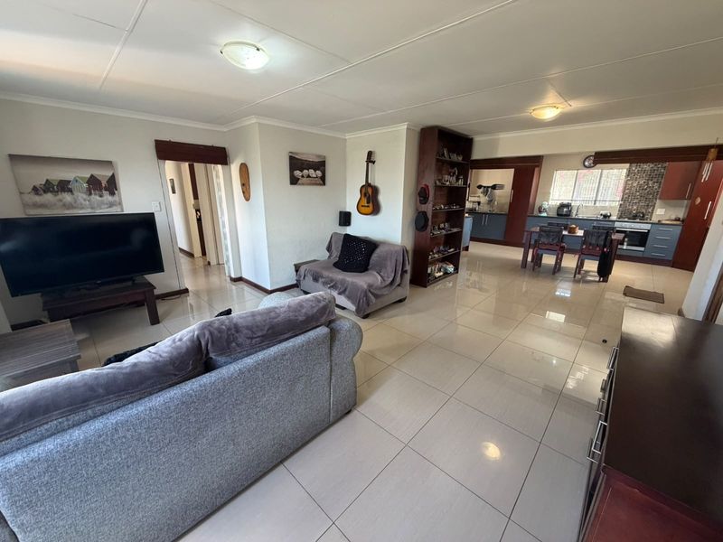 Spacious open-plan living area featuring large format floor tiles, flowing into a functional kitchen with built-in cabinetry and modern appliances.