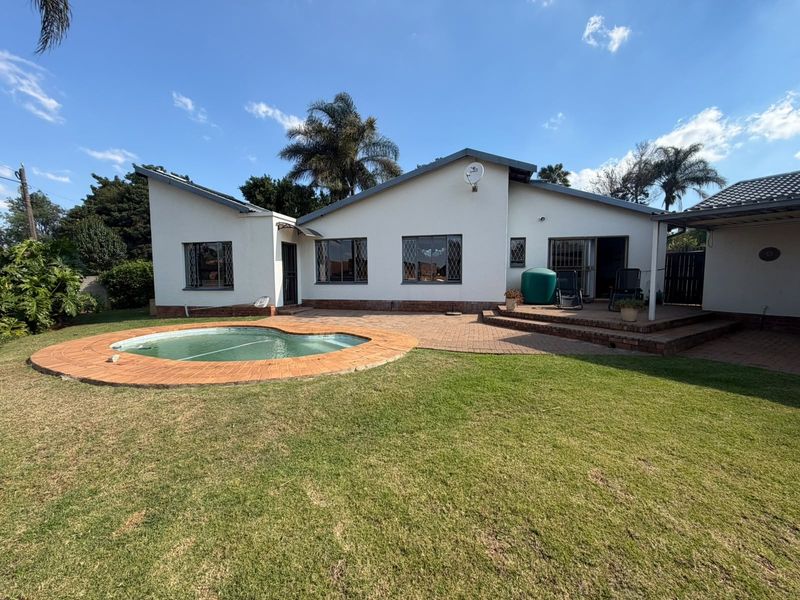 Rear view of the house featuring a swimming pool, brick paved patio area, and a spacious lawn.