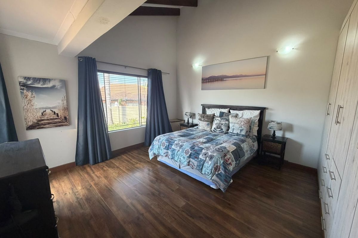 Spacious bedroom featuring high vaulted ceilings with exposed timber beams, laminate flooring, and ample built-in wardrobe storage.