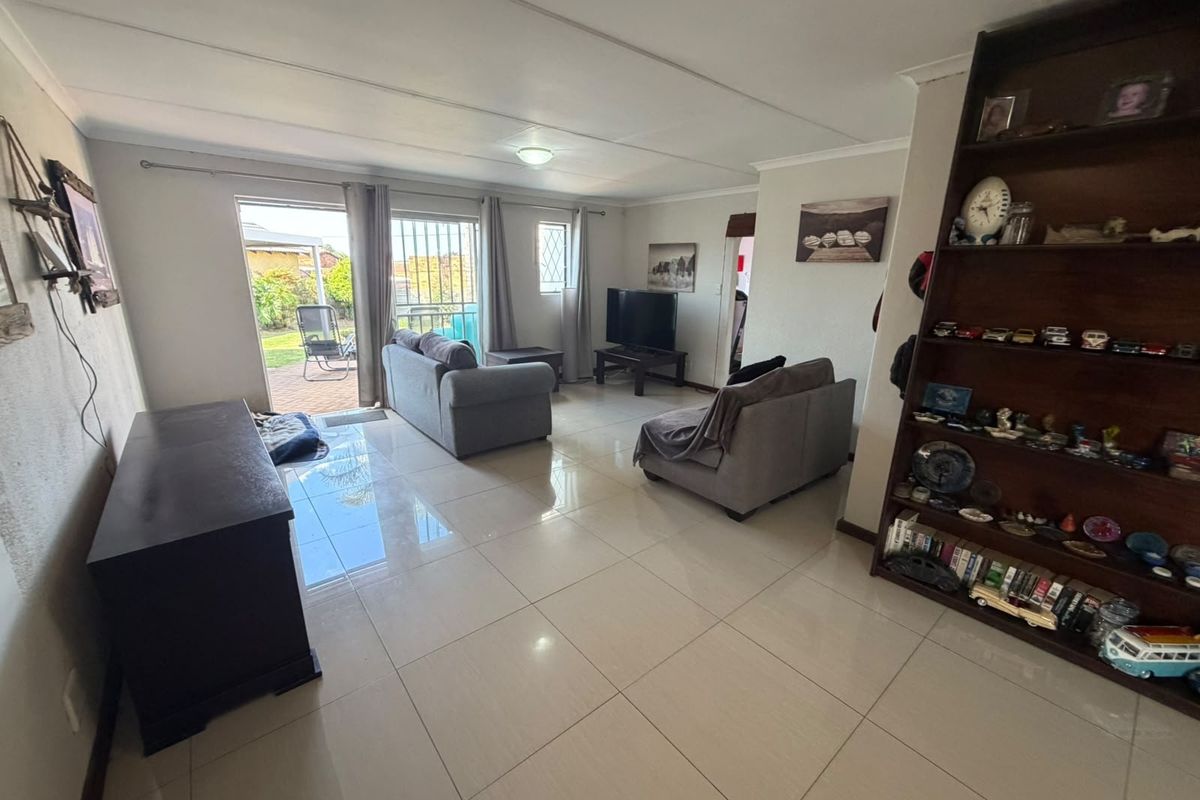 A spacious living room featuring large format floor tiles and a sliding glass door providing direct access to the rear patio and garden.