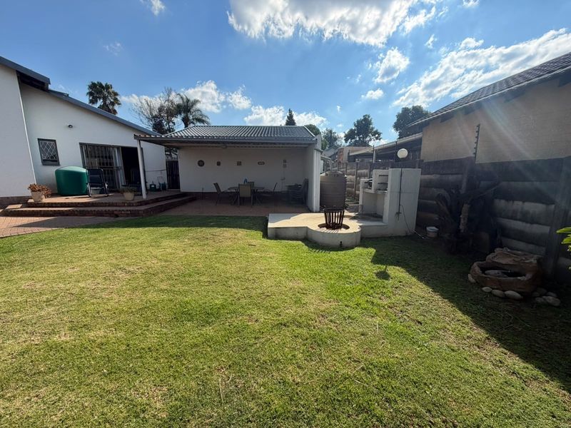 Spacious rear garden featuring a covered patio, built-in braai area, paved terrace, and established lawn, ideal for outdoor entertaining.