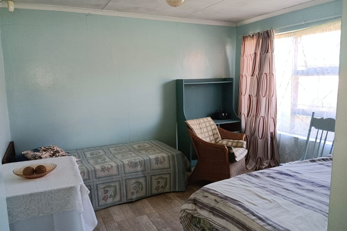 A bedroom featuring tiled flooring and a window, showing signs of wear including visible cracks in the wall plaster.