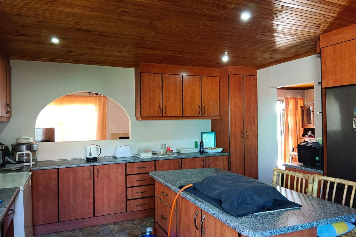 A functional kitchen featuring wooden ceiling paneling, granite countertops, ample built-in cabinetry, and a central island, with an open archway connecting to adjacent living space.