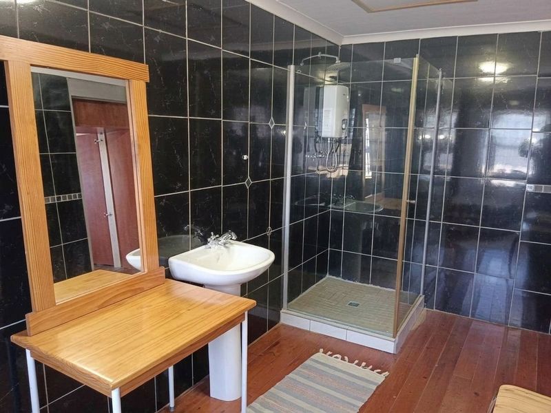 Bathroom featuring black wall tiles, a pedestal basin, and a glass-enclosed shower unit with an electric shower head.