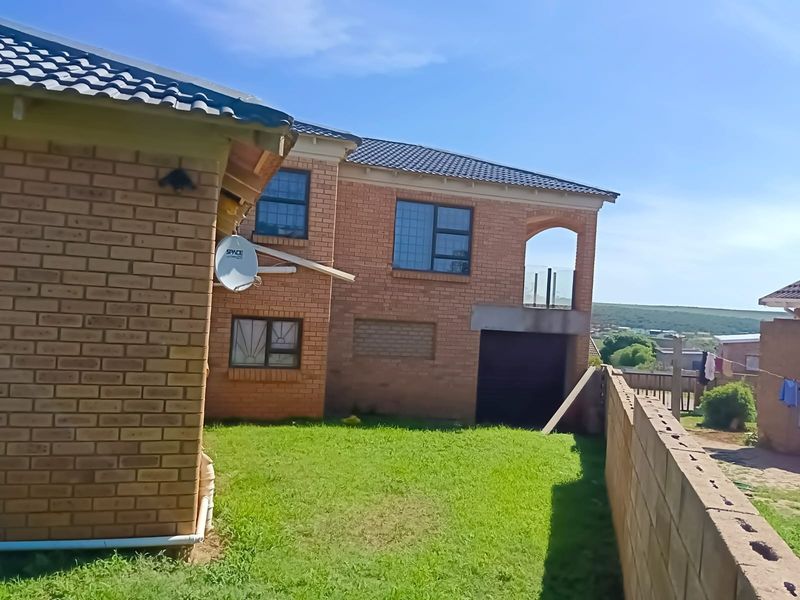 Rear view of a double-story face brick house featuring a balcony, garage access, and a private garden area with boundary walling.